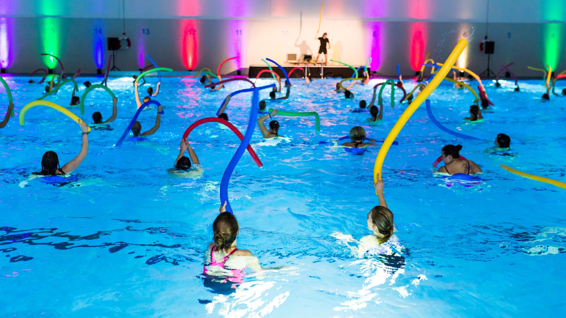 Teilnehmer der blu.AquaNacht schwingen im Schwimmbecken mit den Poolnudeln durch die Luft, © SekundenstillFotografie