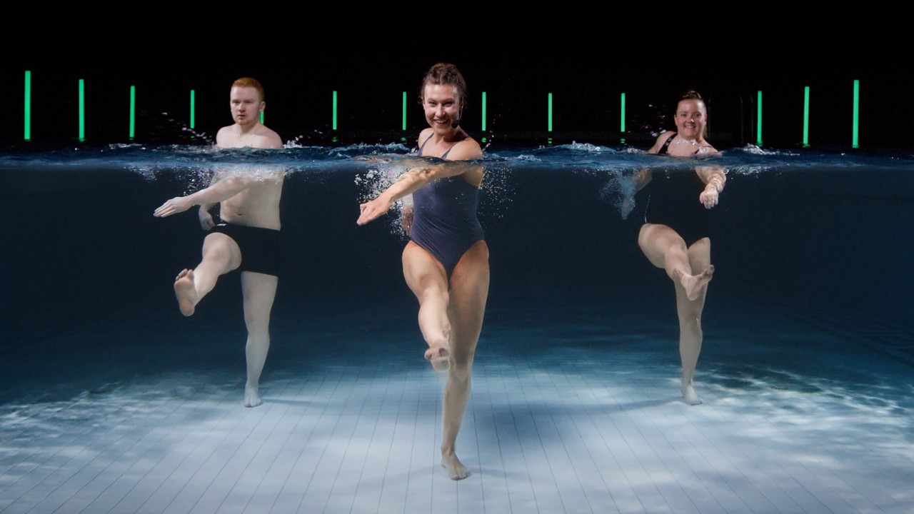 Aquafitness im Schwimmbad: Drei Personen trainieren im Wasser bei einem virtuellen Hydrohex-Kurs mit synchronen Beinbewegungen und moderner Beleuchtung