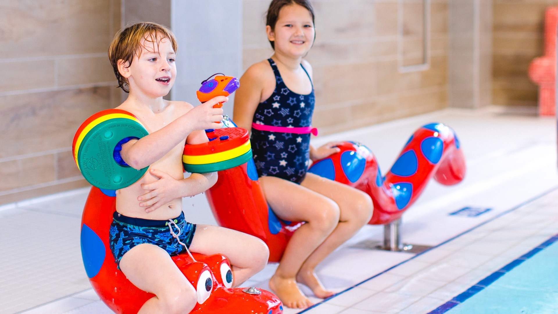 Zwei Kinder sitzen im Kiezbad auf der roten Wasserschlange, © Alena Suber