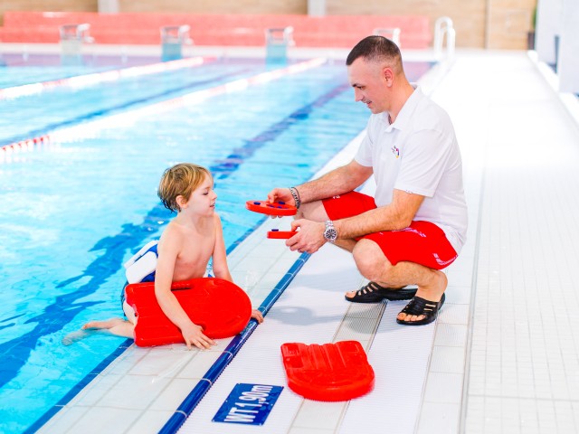 Schwimmlehrer im Kiezbad erklärt Kind die Schwimmhilfen, © Alena Suber