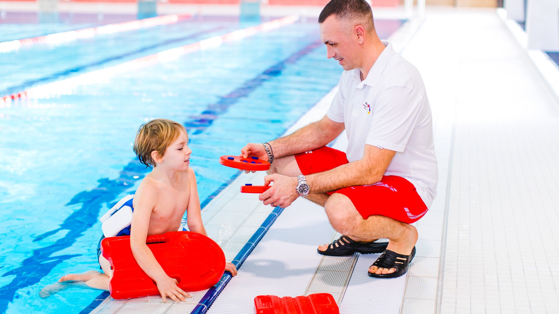 Schwimmlehrer im Kiezbad erklärt Kind die Schwimmhilfen, © Alena Suber