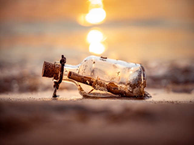 Flaschenpost am Strand vor der untergehenden Sonne