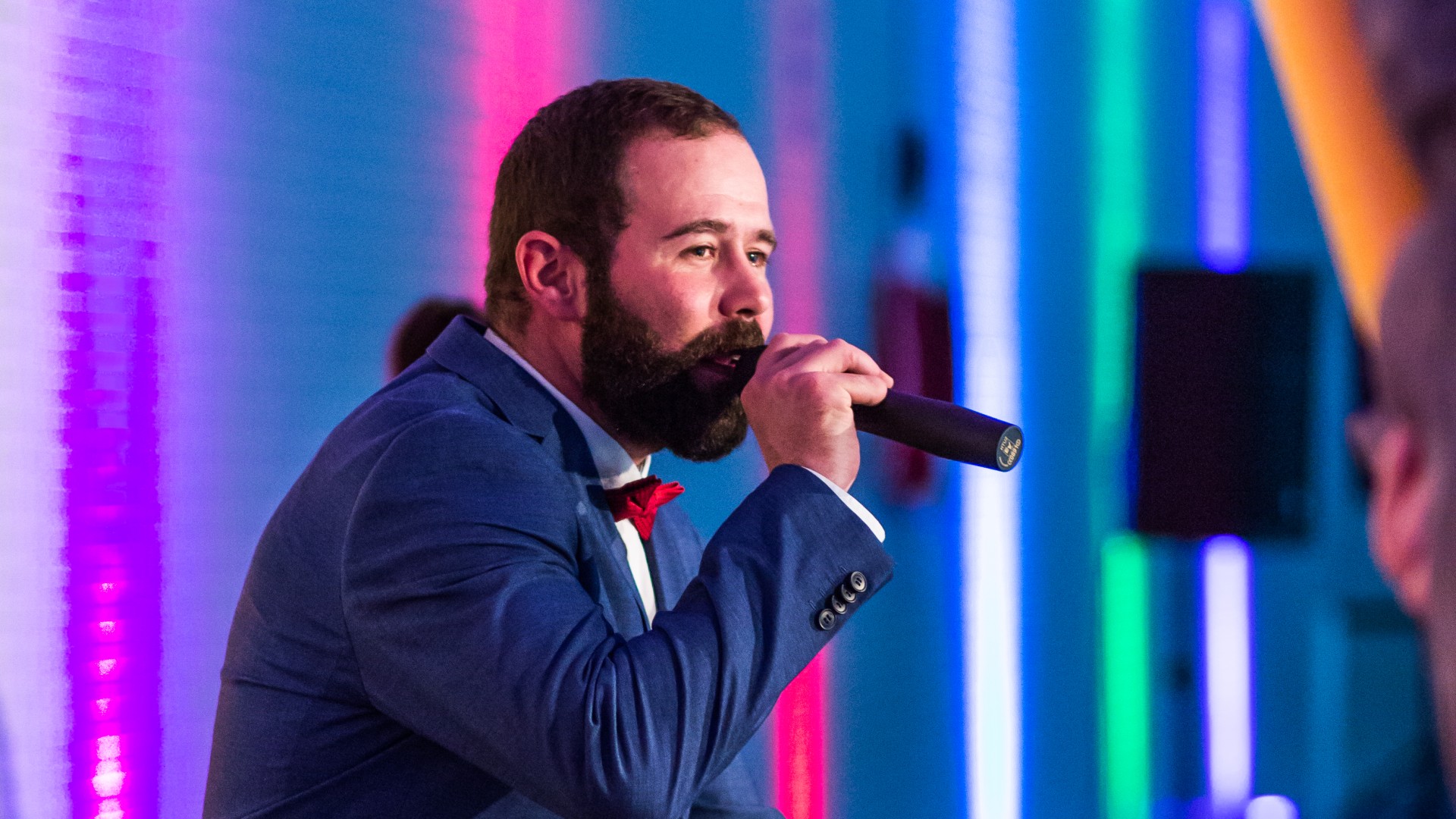 Trainer im Anzug singt mit dem Mikrofon vor dem Mund auf der blu.AquaNacht, © SekundenstillFotografie