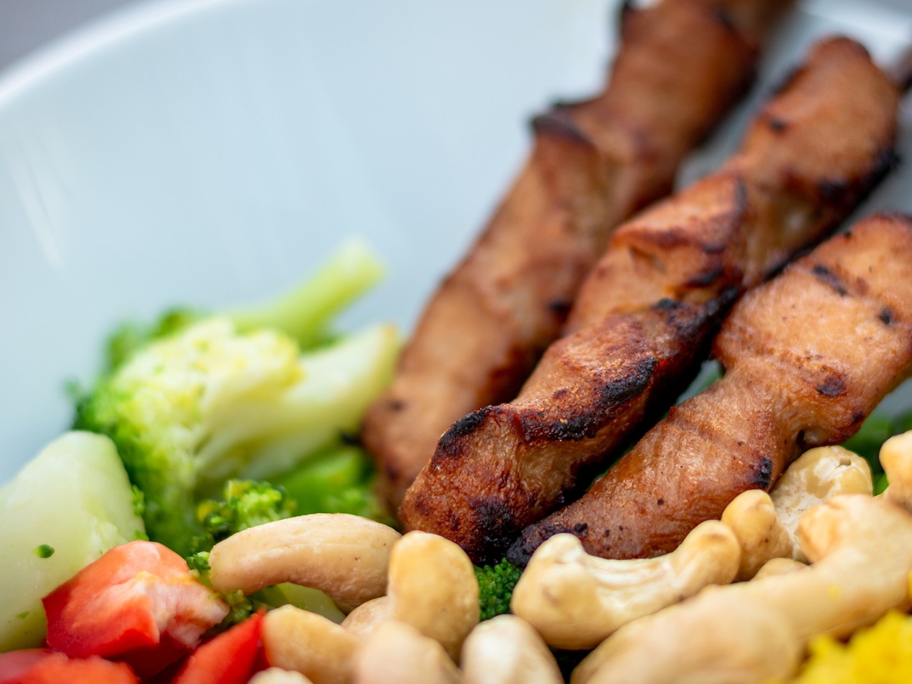 Bowl mit drei Hähnchenspießen, Cashewkernen und Gewmüse