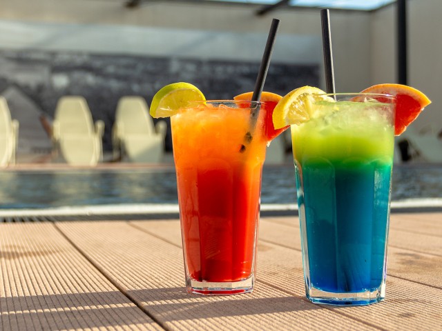 Ein roter und blauer Cocktail stehen am Beckenrand in der Sonne auf der Dachterasse im blu