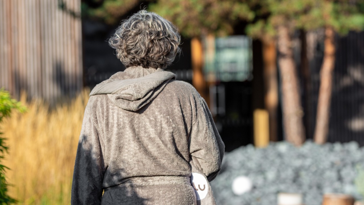 Frau im Bademantel mit Handtuch unter dem Arm auf der Dachterasse im blu