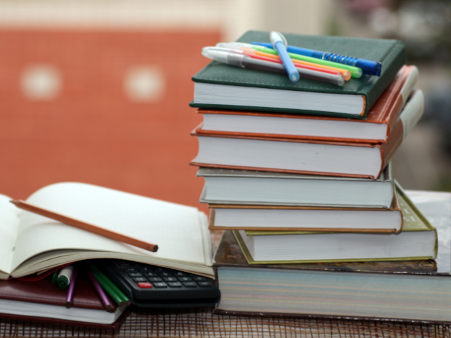 ein aufgeschlagenes Buch, daneben liegt ein Stapel Bücher