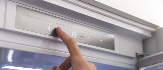 Eine Person ändert die Temperatur eines Kühlschranks, © AdobeStock_339166513