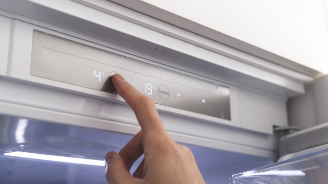 Eine Person ändert die Temperatur eines Kühlschranks, © AdobeStock_339166513