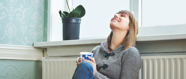 Junge Frau lehnt sich mit dem Rücken an warmer Heizung an, © m-imagephotography /iStock