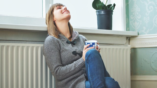 Junge Frau lehnt sich mit dem Rücken an warmer Heizung an, © m-imagephotography /iStock