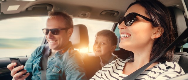 eine gute gelaunte Familie fährt in einem Auto. Der Beifahrer hat ein Handy in der Hand, © AdobeStock