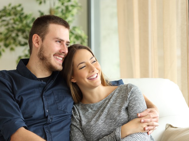 Lächelndes junges Pärchen sitzt zu Hause in Potsdam auf der Couch, © Antonioguillem /Fotolia