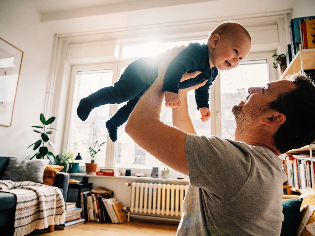 Papa streckt kleines Baby in der Wohnstube mit beiden Armen in die Luft