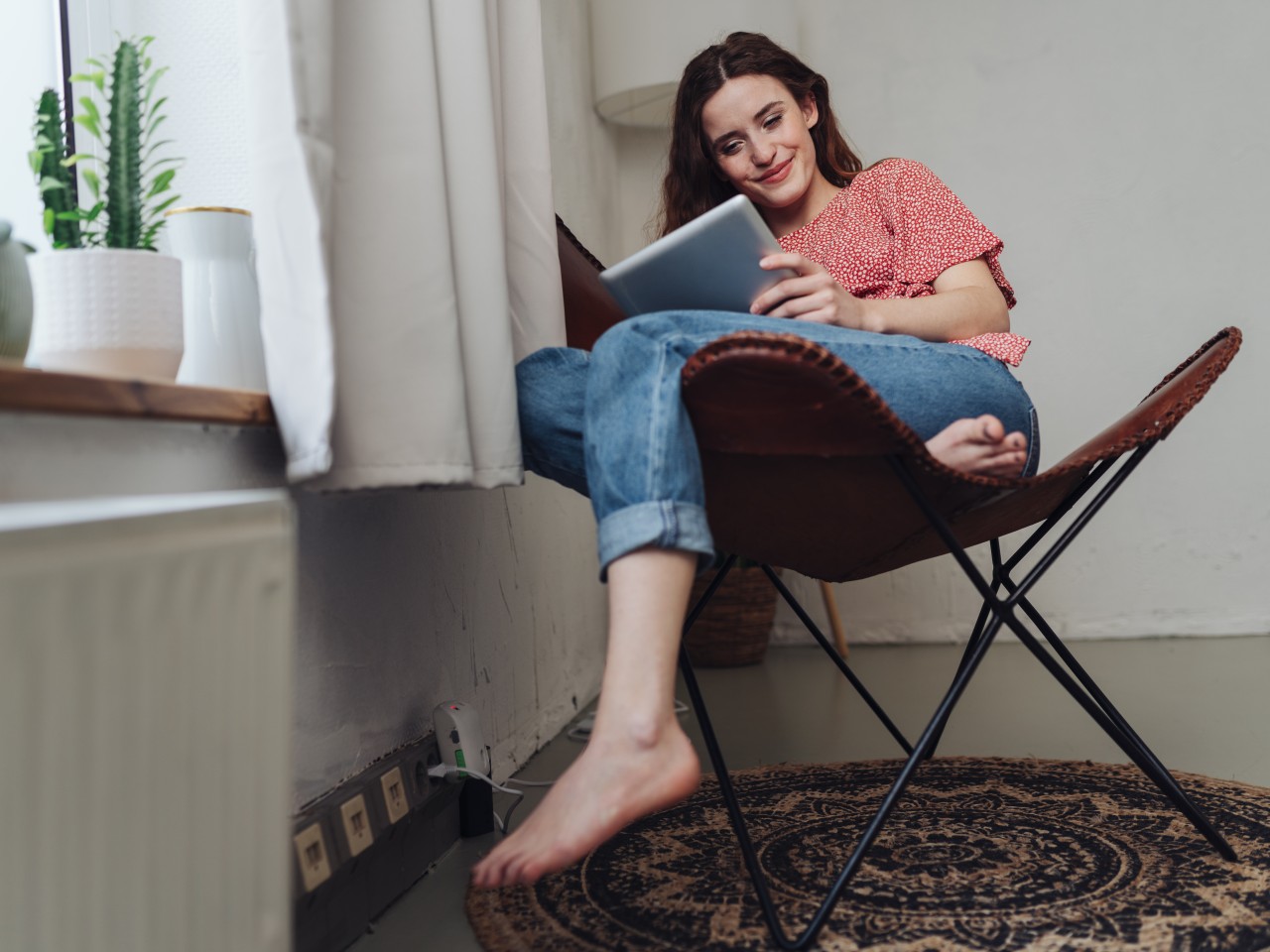 Junge Frau sitzt barfuß auf dem Ledersessel und schaut auf ihr Tablet, © contrastwerkstatt – stock.adobe.com