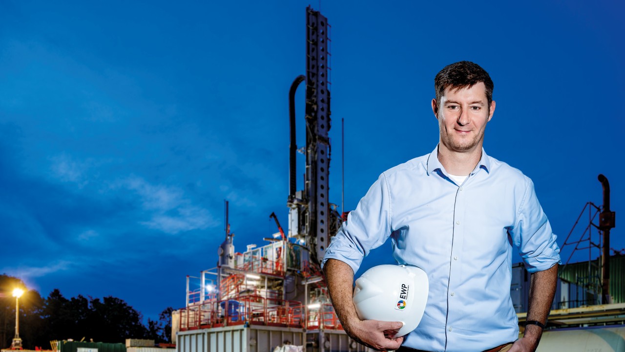 Ingenieur mit Bauhelm in der Hand steht vor Baustelle der Geothermieanlage