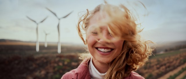 Junge Frau auf dem Feld mit Windrädern weht der Wind durch das Haar