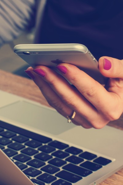 Frau sitzt am Schreibtisch vor dem Laptop und hält ihr Smartphone in der Hand