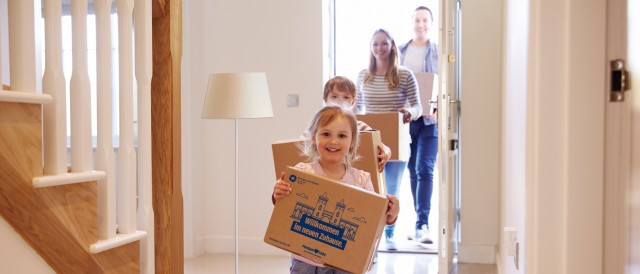 Junge Famiile betritt neue Wohnung mit Umzugkartons in den Händen