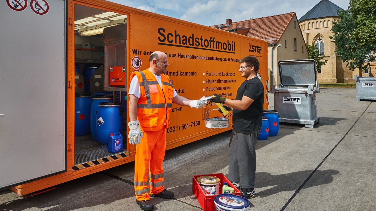 Ein Kunde übergibt am STEP-Schadstoffmobil einem STEP-Mitarbeiter einen flachen Farbeimer und Öl