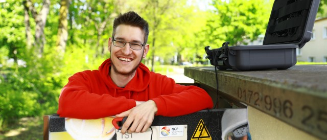 Junger Student der Industriellen Elektrotechnik mit rotem Hoodie steht an einer Trafostation, © Katheeln Friedrich