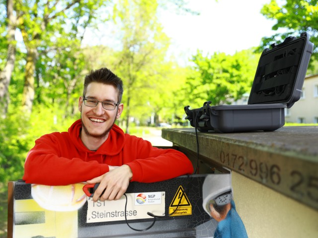 Junger Student der Industriellen Elektrotechnik mit rotem Hoodie steht an einer Trafostation, © Katheeln Friedrich