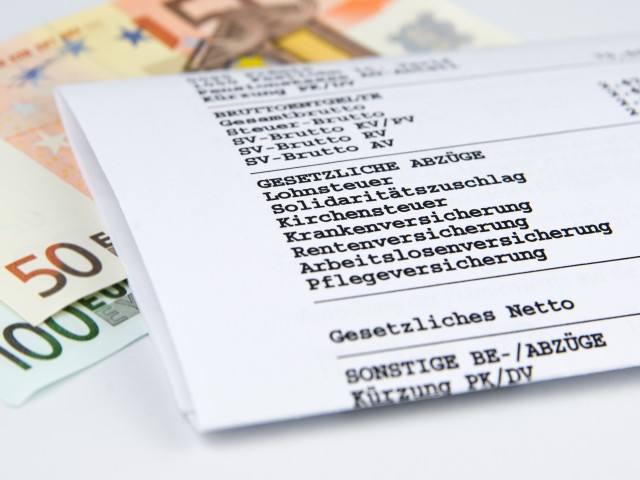Lohn- und Gehaltsabrechnungszettel, darunter liegt Geld
