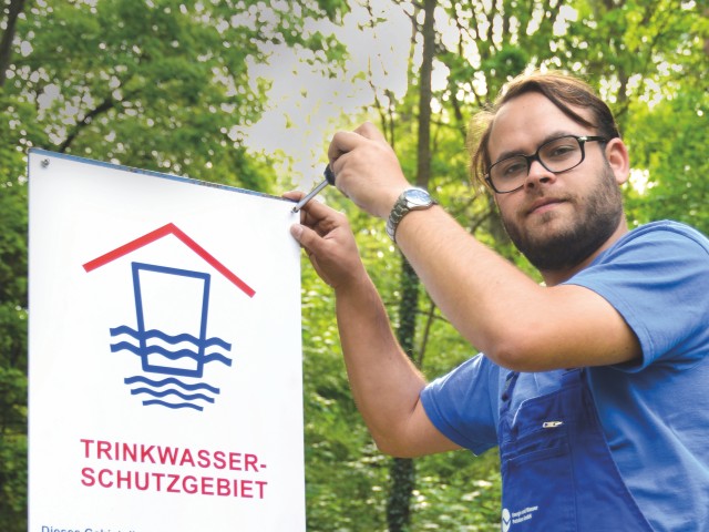 Mitarbeiter der Energie und Wasser Potsdam montiert ein Trinkwasserschutzgebiet-Schild vor einem Brunnen, © Sabeth Stickforth