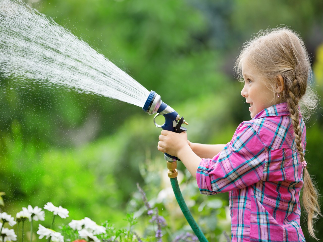 Mädchen mit Gartenschlauch spritzt Wasser im Garten