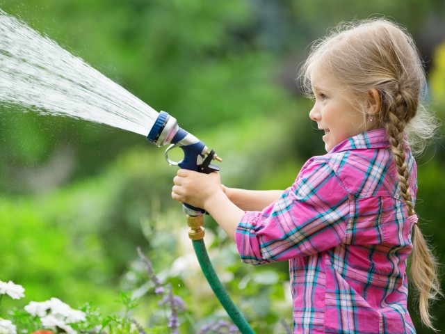 Mädchen mit Gartenschlauch spritzt Wasser im Garten