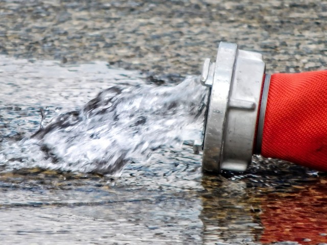 Löschwasser läuft am Ende eines roten Feuerwehrschlauches auf die Straße